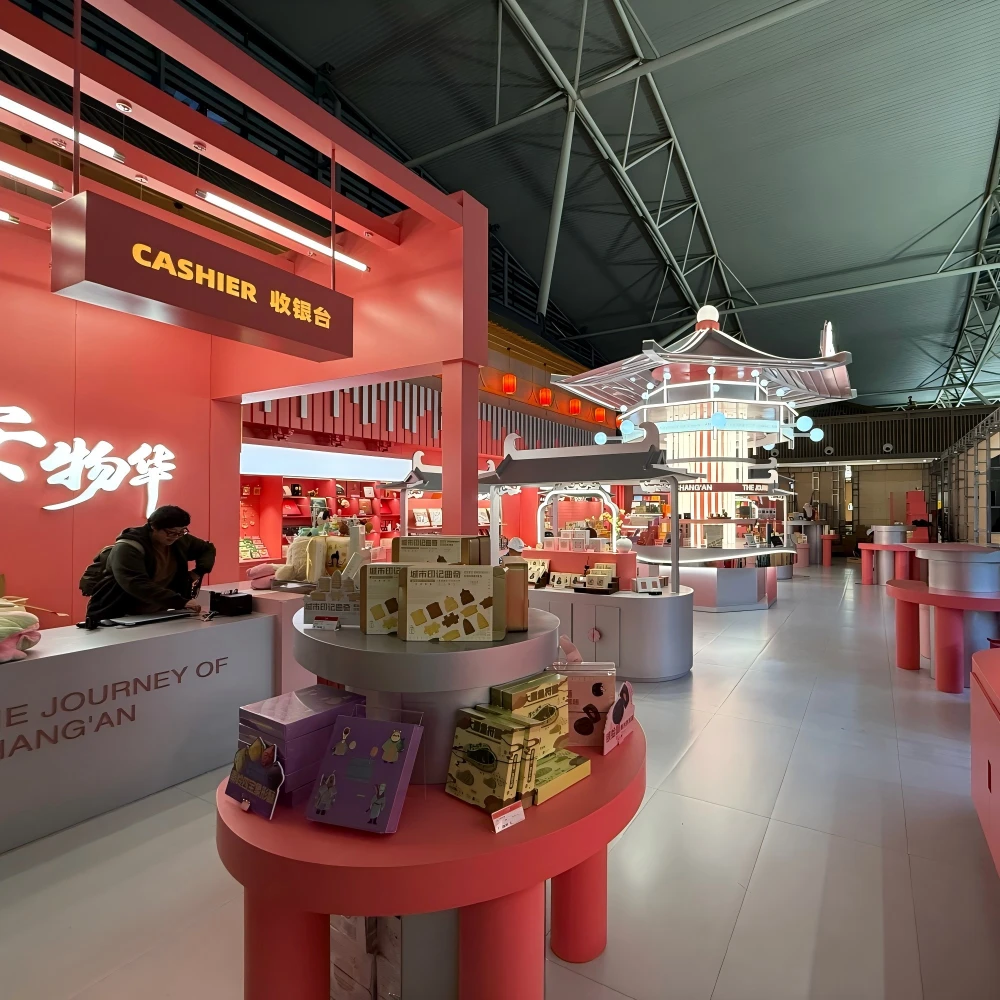 Wide-angle concourse view of coral-red retail island with continuous display walls and central pavilion in a retail store layout design airport island