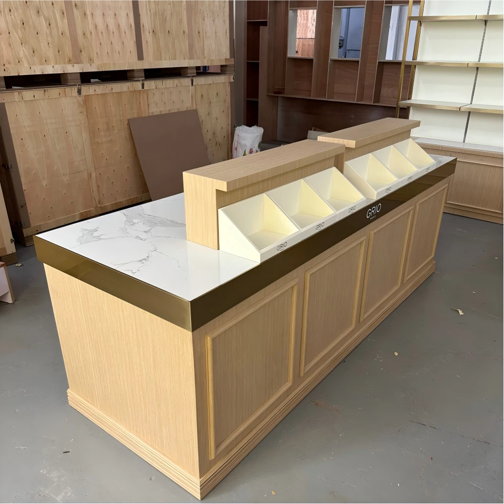 Sloped-bin merchandising counter with light-oak body, champagne-gold edge banding and white marble-look top in a retail design and build production sample