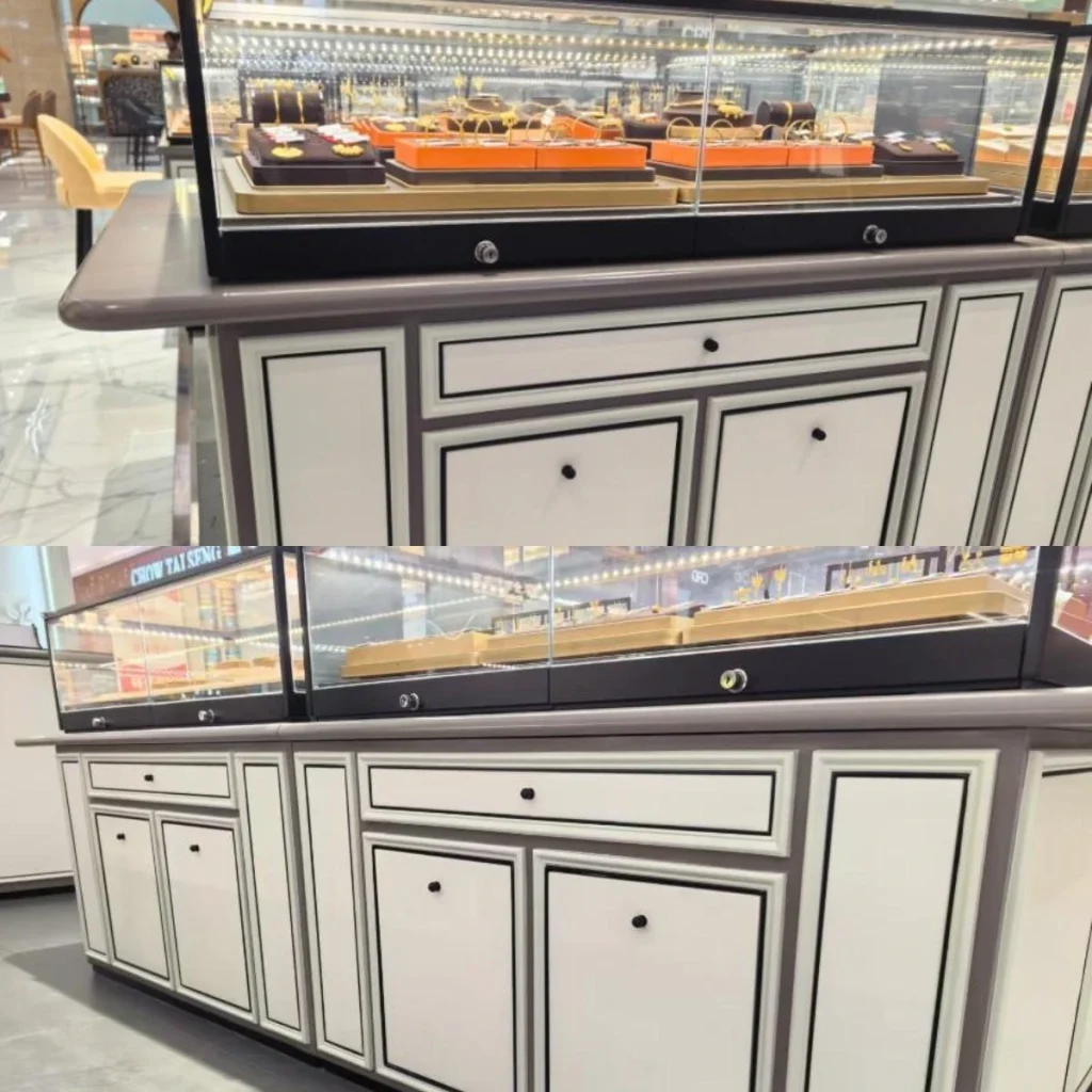 Black jewelry display cases in a mall: black metal frames over white French-panel casework, gold chains and bracelets on velvet trays