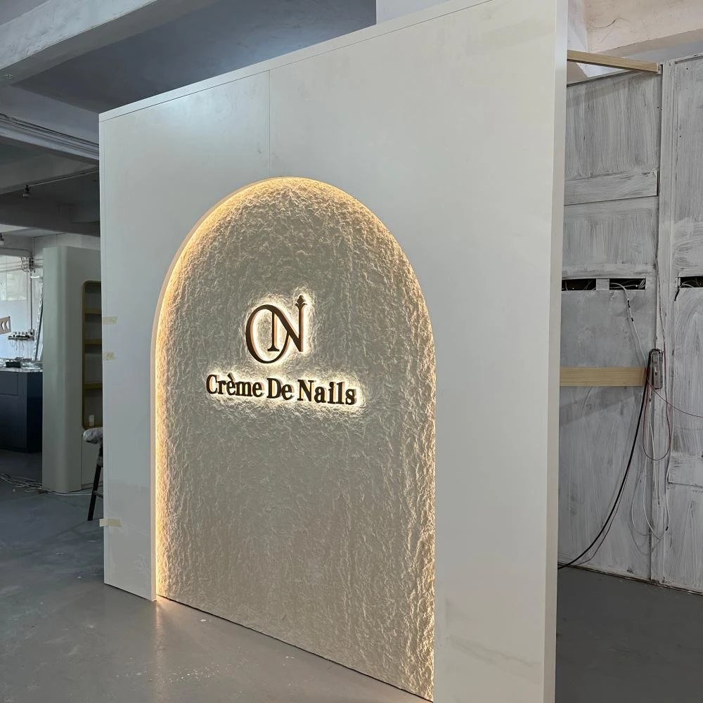 Stone-textured archway with rose-gold wordmark and concealed LED halo, freestanding nail salon entrance installation sample