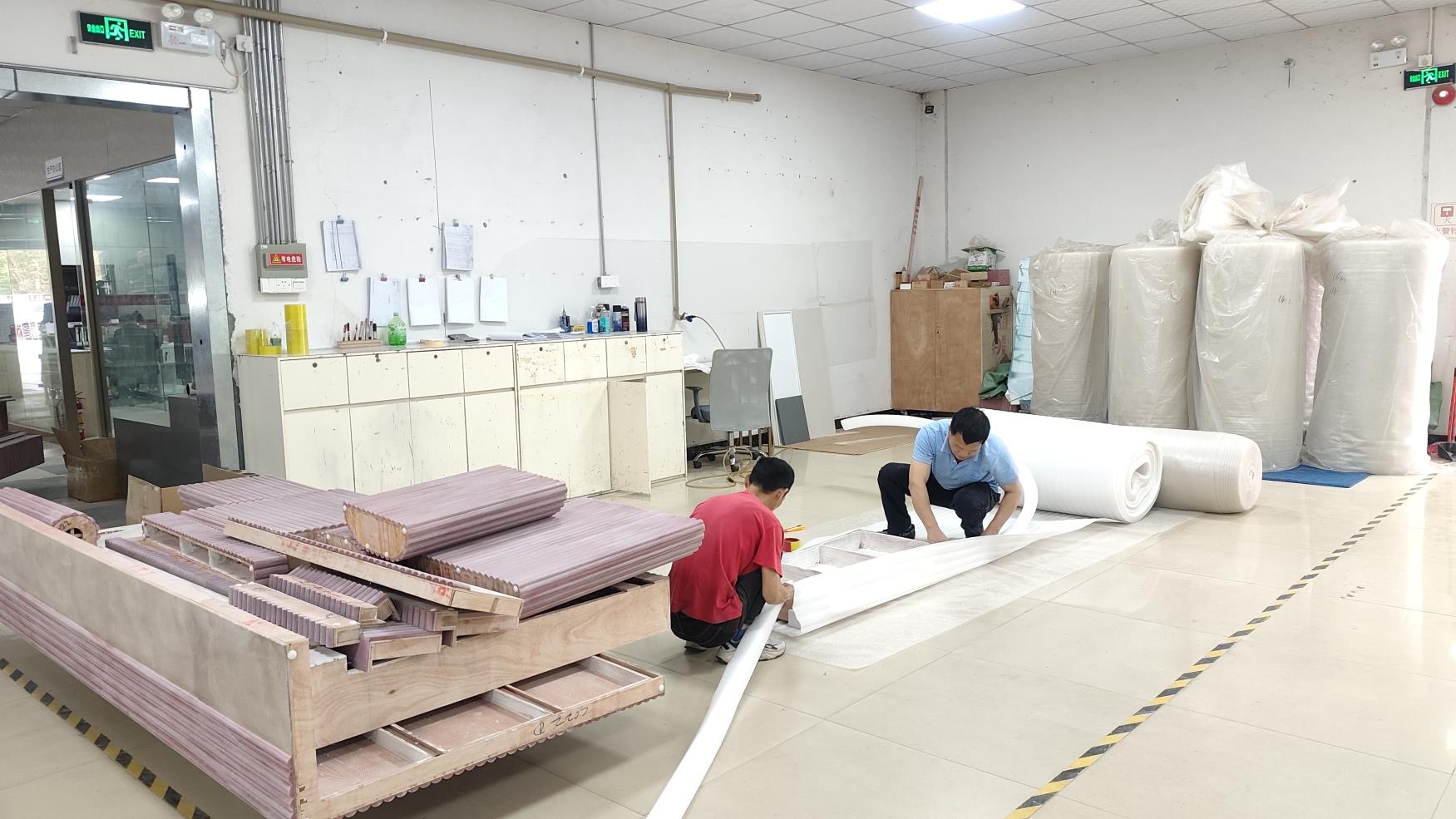 workers flat-packing display case components into a wooden crate with foam