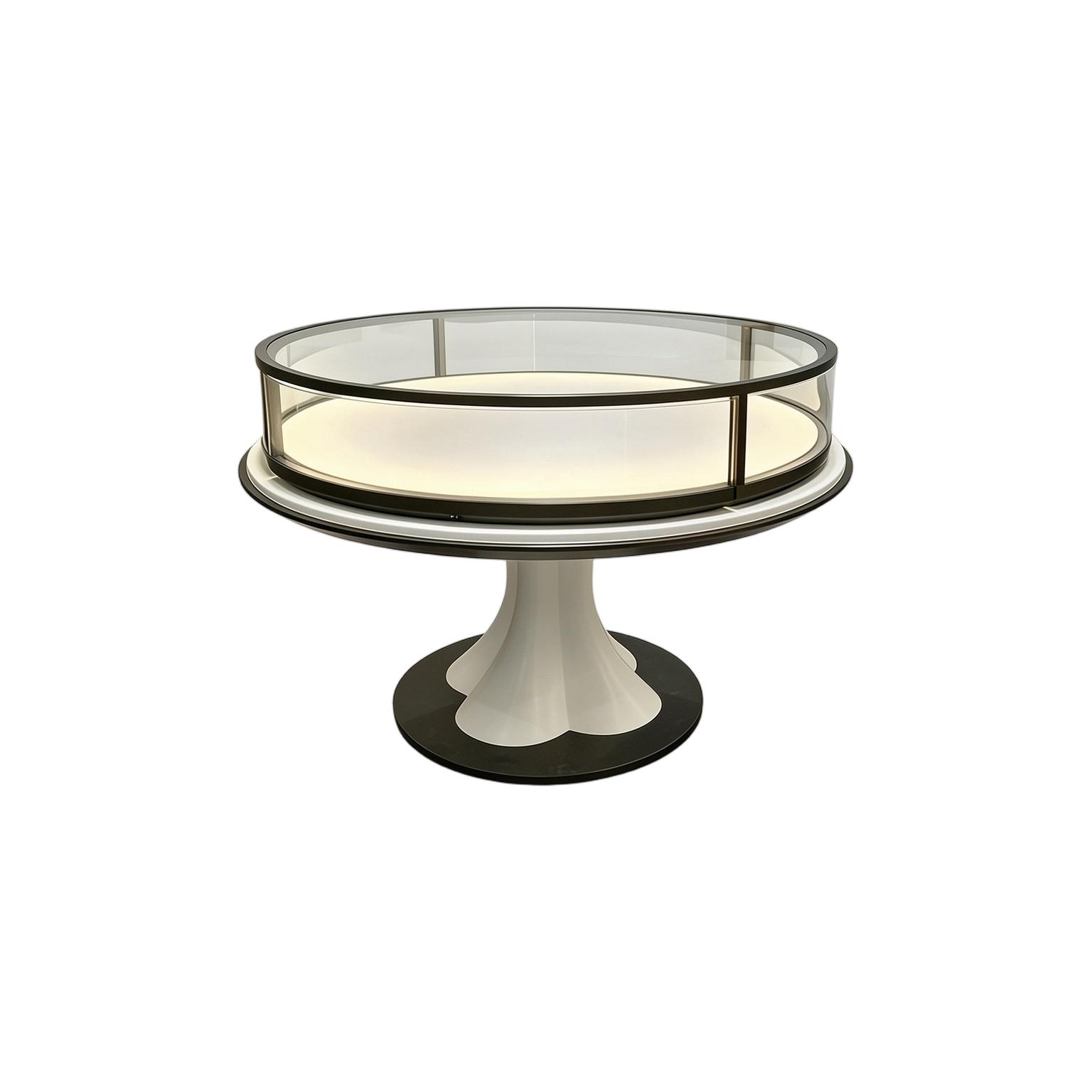Round display table with an illuminated deck, clear glass rail and white pedestal base, on a white background