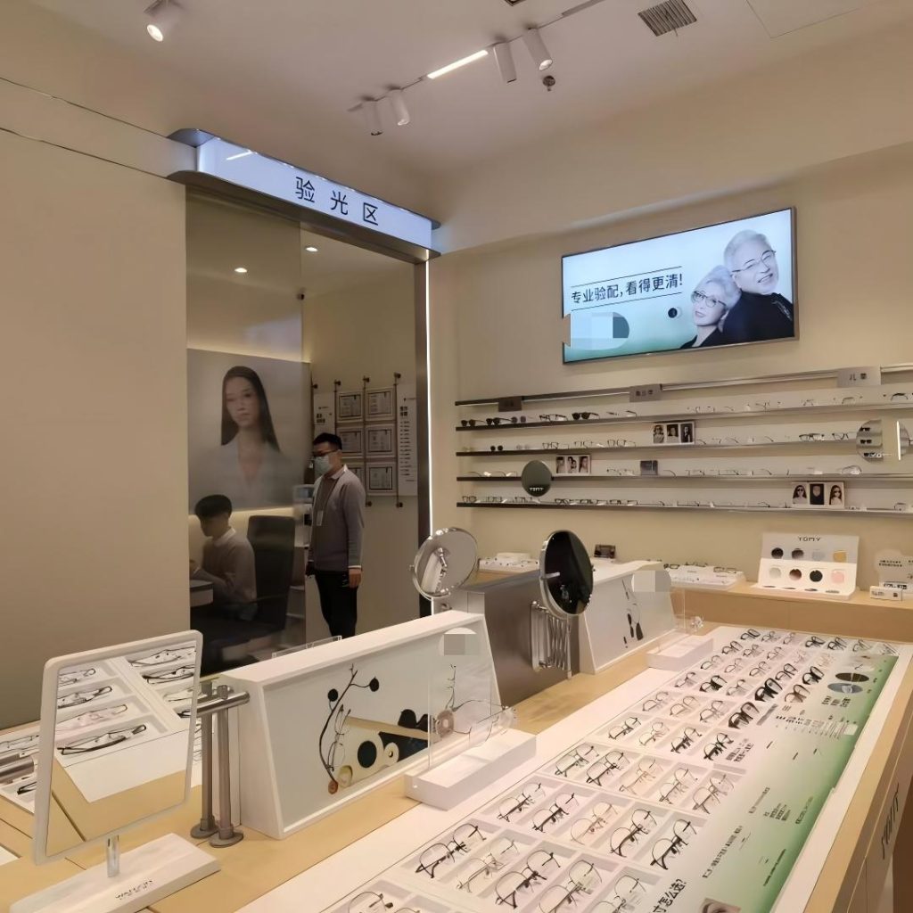Arc sunglass display wall with face-out frames and portrait cards under lit shelving in an open-front eyewear store