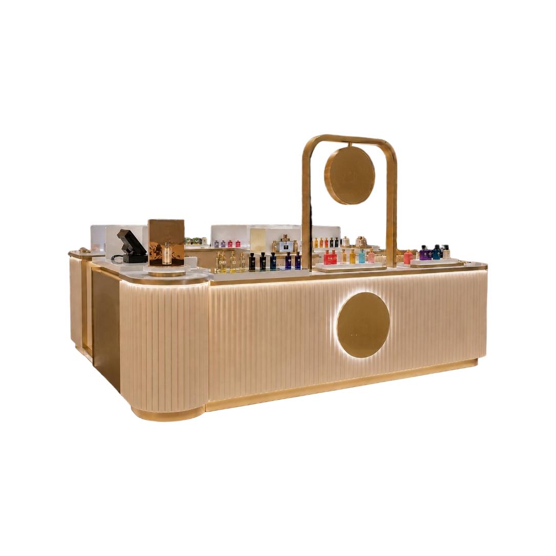 champagne gold fluted mall display kiosk on white background with glowing round logo panel and stepped stone counter full of perfume bottles